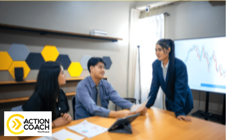 Three people have a business meeting in a modern office, discussing a line graph on a large monitor. The ActionCoach Northwest logo appears at the bottom left, highlighting their 12-week MasterCLASS for Management Mastery.
